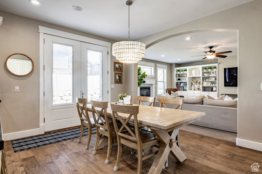 Dining room featuring baseboards, hardwood / wood-style flooring, ceiling fan, a glass covered fireplace, and arched walkways