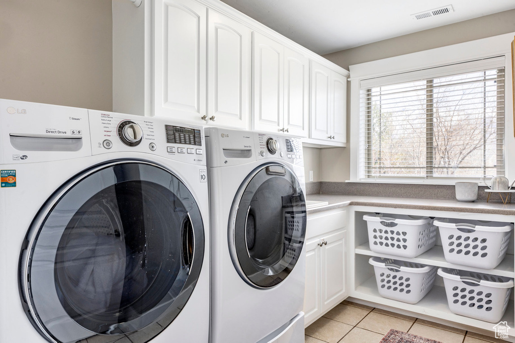 Laundry area featuring washing machine and clothes dryer, cabinet space, and light tile patterned floors