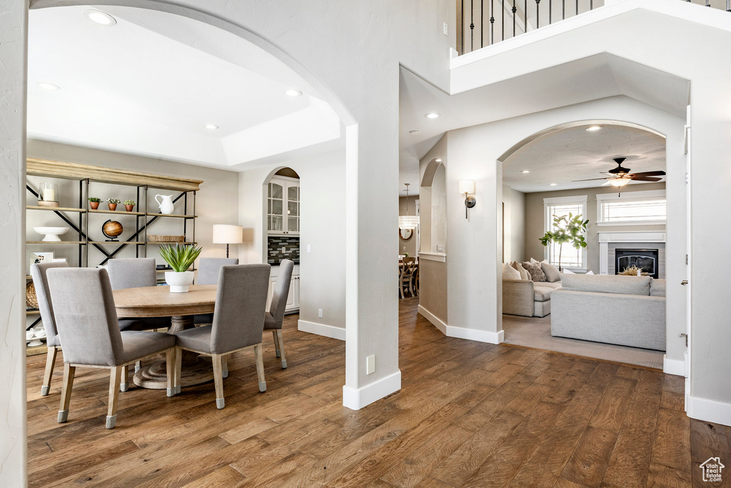 Dining space featuring ceiling fan, arched walkways, wood finished floors, baseboards, and a glass covered fireplace