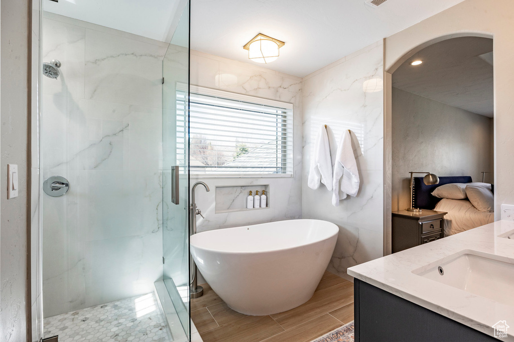 Full bath featuring vanity, a marble finish shower, a soaking tub, and wood tiled floors