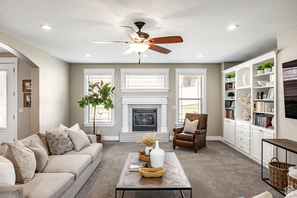 Carpeted living area featuring arched walkways, a ceiling fan, a glass covered fireplace, baseboards, and recessed lighting