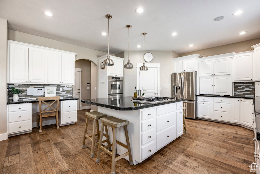 Kitchen with stainless steel appliances, backsplash, dark wood finished floors, arched walkways, and dark countertops