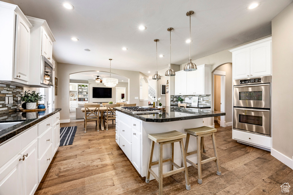 Kitchen with appliances with stainless steel finishes, arched walkways, tasteful backsplash, a center island, and light wood finished floors