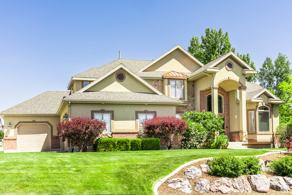 View of front of house featuring stucco siding, a garage, a front lawn, and brick siding