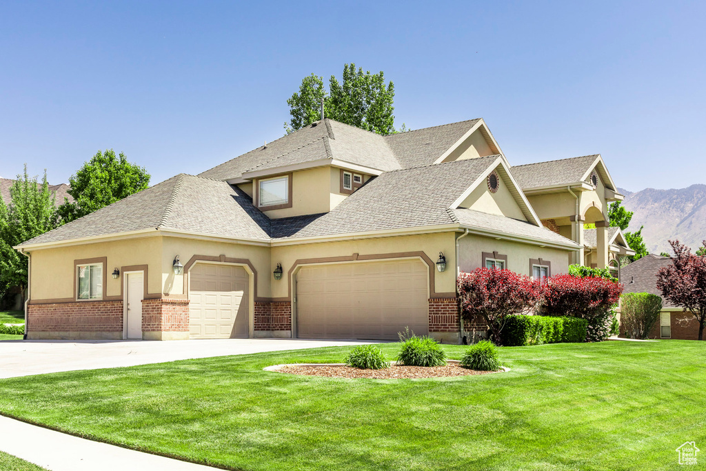 View of front of home featuring an attached garage, a front lawn, stucco siding, and brick siding