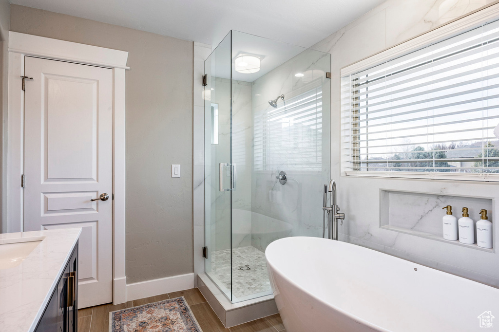 Bathroom featuring a freestanding bath, a shower stall, wood finished floors, vanity, and baseboards