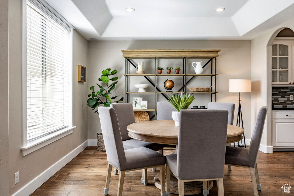 Dining room with a tray ceiling, baseboards, dark wood finished floors, recessed lighting, and arched walkways