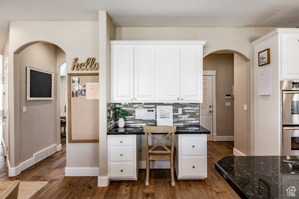 Kitchen featuring arched walkways, stainless steel double oven, white cabinets, baseboards, and dark stone countertops