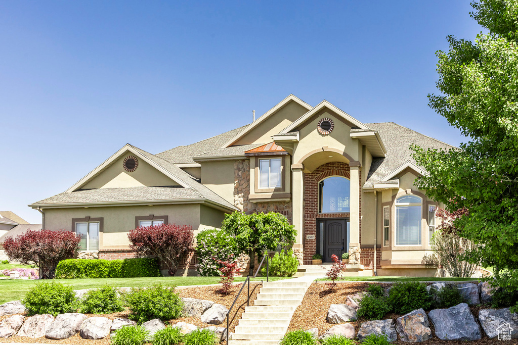 View of front of house featuring stucco siding, stone siding, brick siding, and roof with shingles