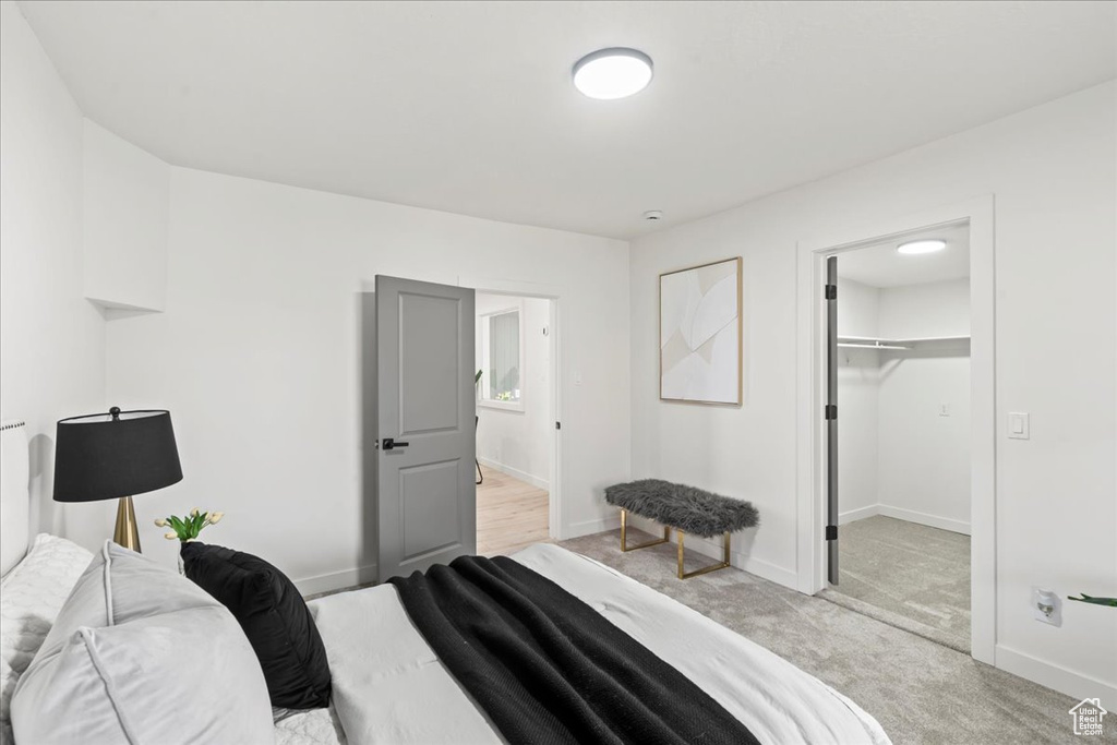 Bedroom with a walk in closet, baseboards, and light colored carpet
