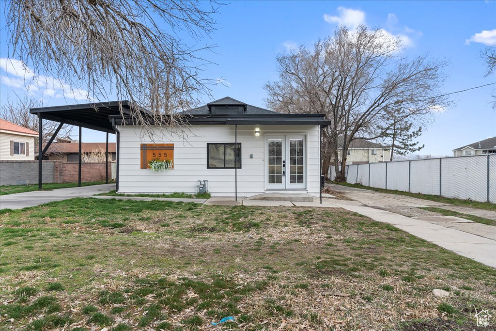 View of front of house featuring a front yard, concrete driveway, french doors, and fence