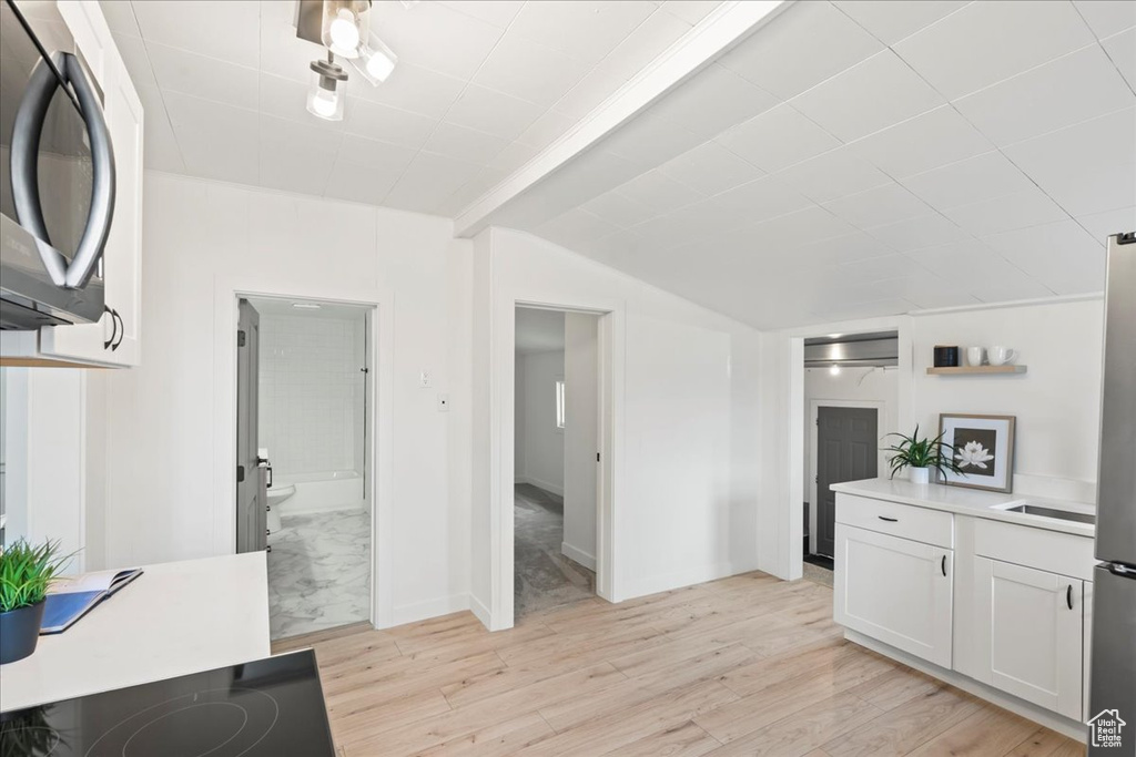 Kitchen with stainless steel microwave, white cabinetry, light countertops, and light wood-style floors