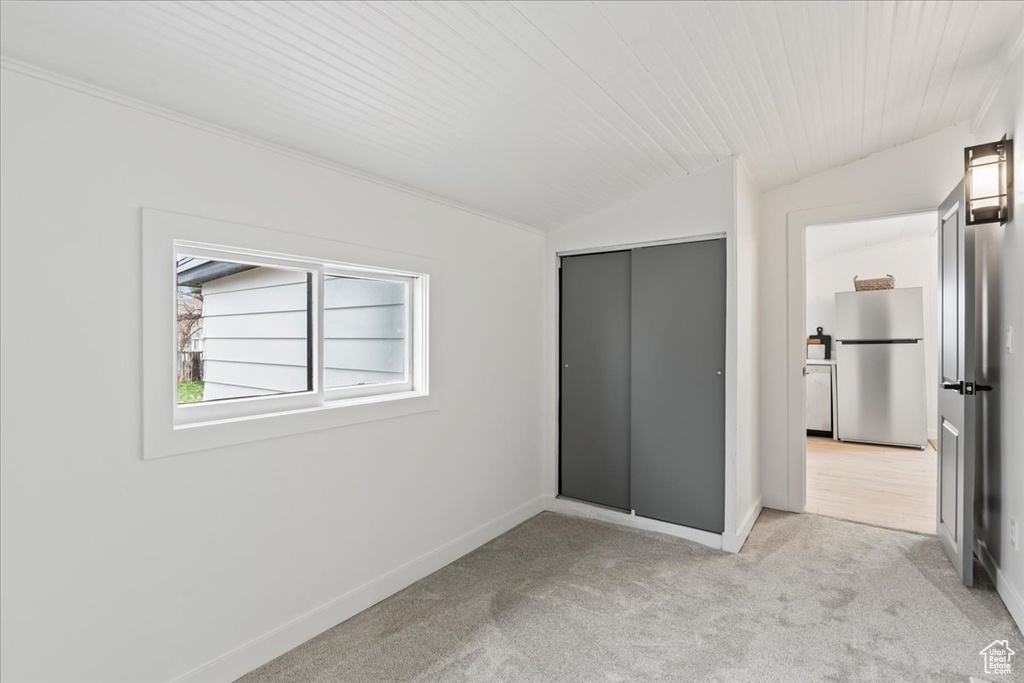 Unfurnished bedroom with baseboards, freestanding refrigerator, vaulted ceiling, a closet, and carpet flooring