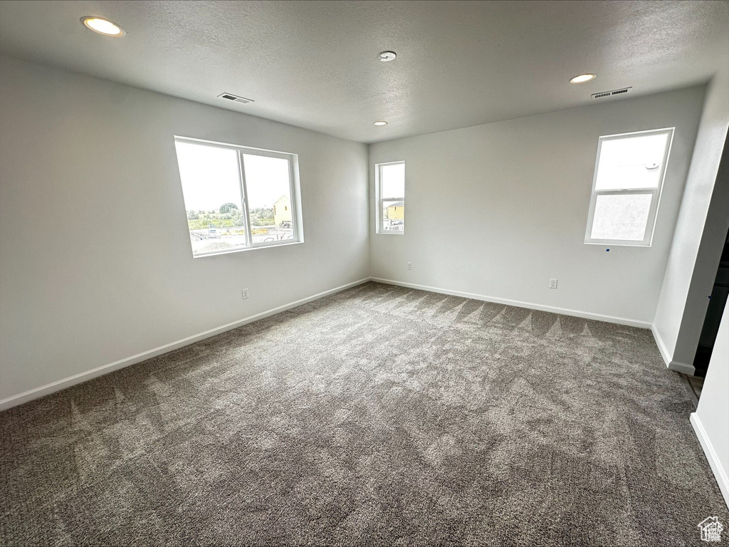 Unfurnished room featuring dark colored carpet, visible vents, baseboards, and a textured ceiling