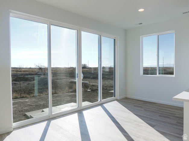Empty room featuring healthy amount of natural light, wood finished floors, recessed lighting, and baseboards