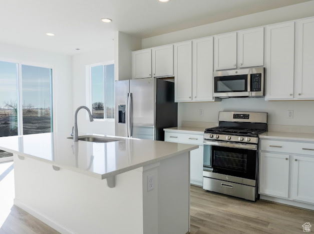 Kitchen with appliances with stainless steel finishes, a sink, a kitchen island with sink, white cabinets, and recessed lighting