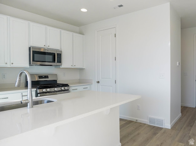 Kitchen featuring stainless steel appliances, light wood finished floors, white cabinets, and recessed lighting
