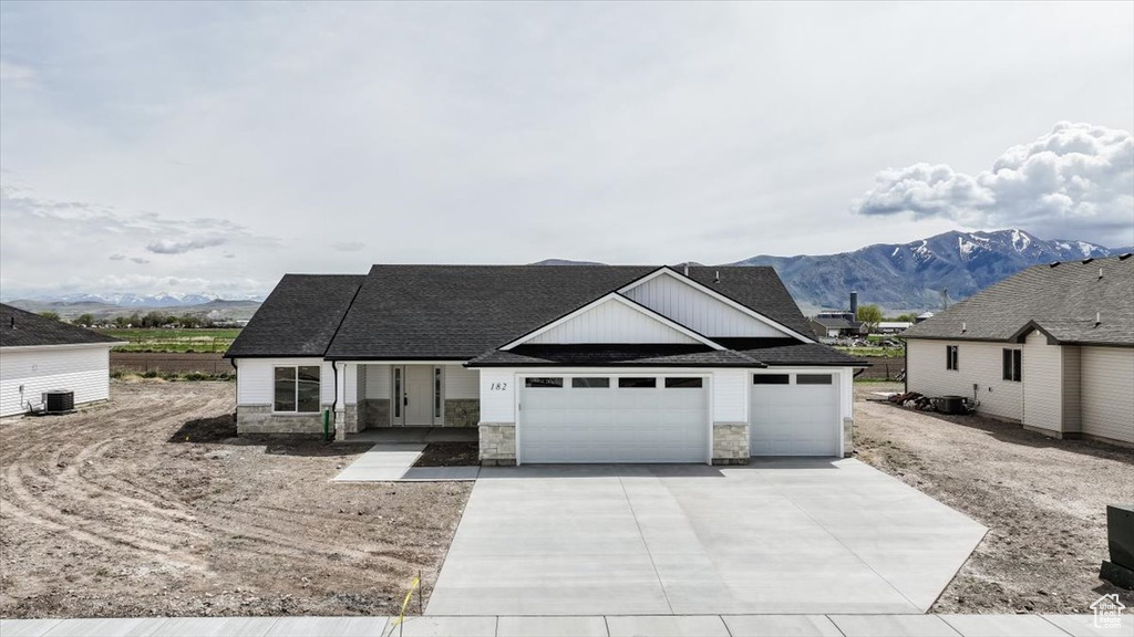View of front of home featuring roof with shingles, an attached garage, stone siding, a mountain view, and driveway