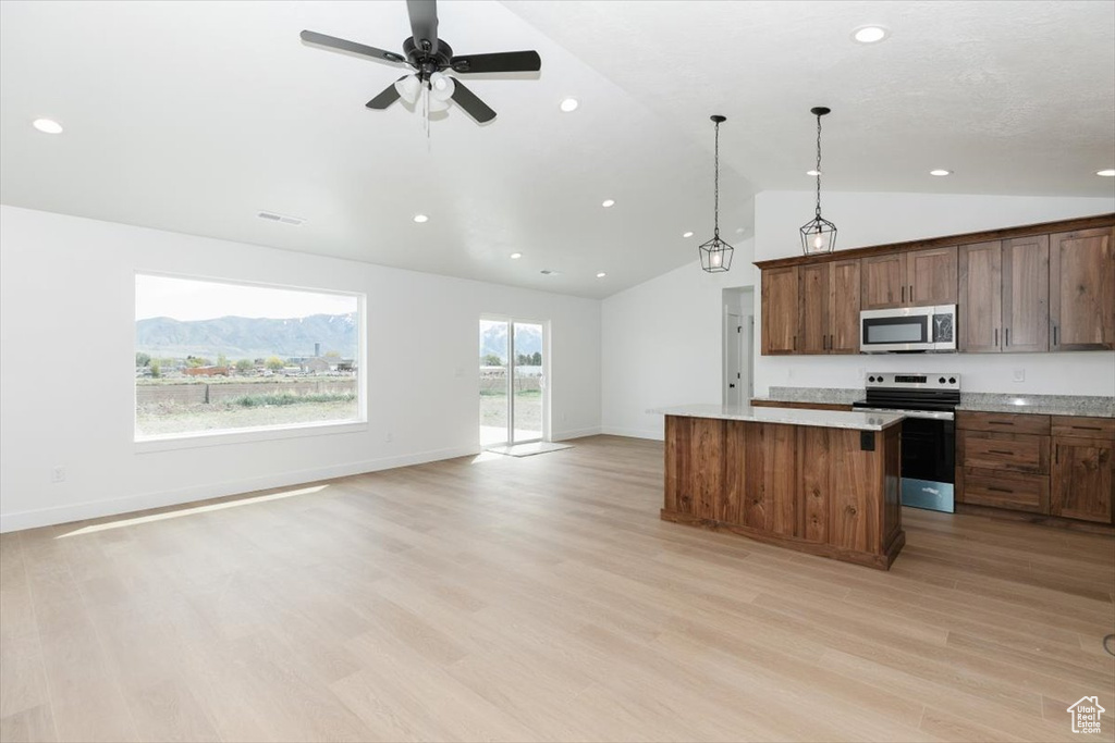 Kitchen featuring appliances with stainless steel finishes, light countertops, open floor plan, lofted ceiling, and a kitchen island