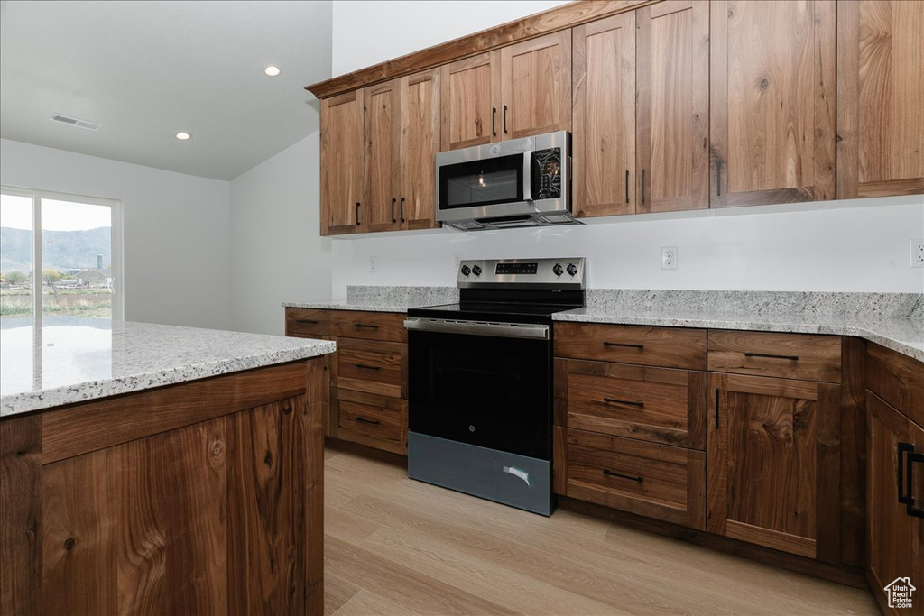 Kitchen featuring visible vents, light stone counters, lofted ceiling, light wood-style floors, and stainless steel appliances