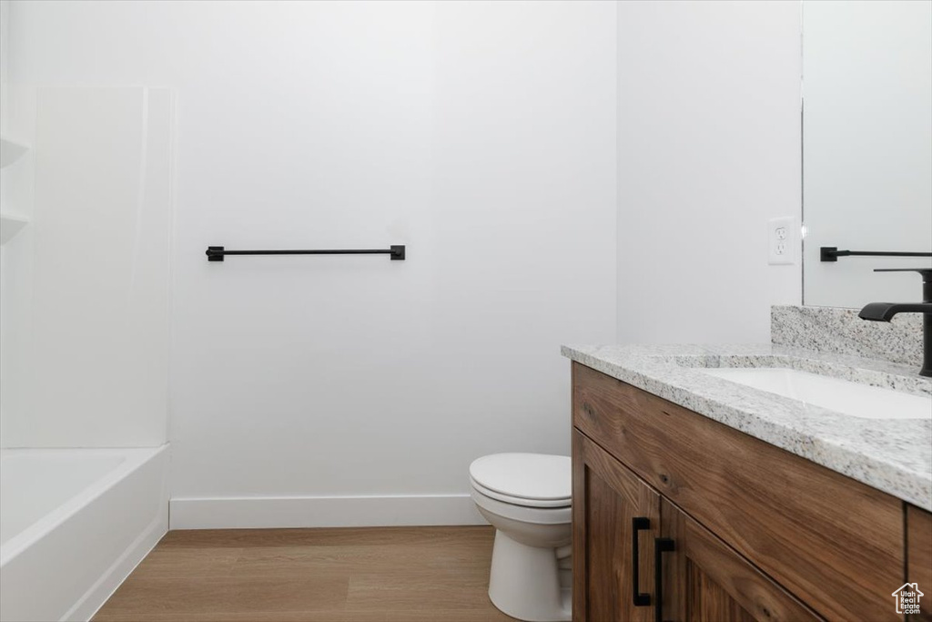 Full bath with vanity, wood finished floors, toilet, baseboards, and a bathing tub