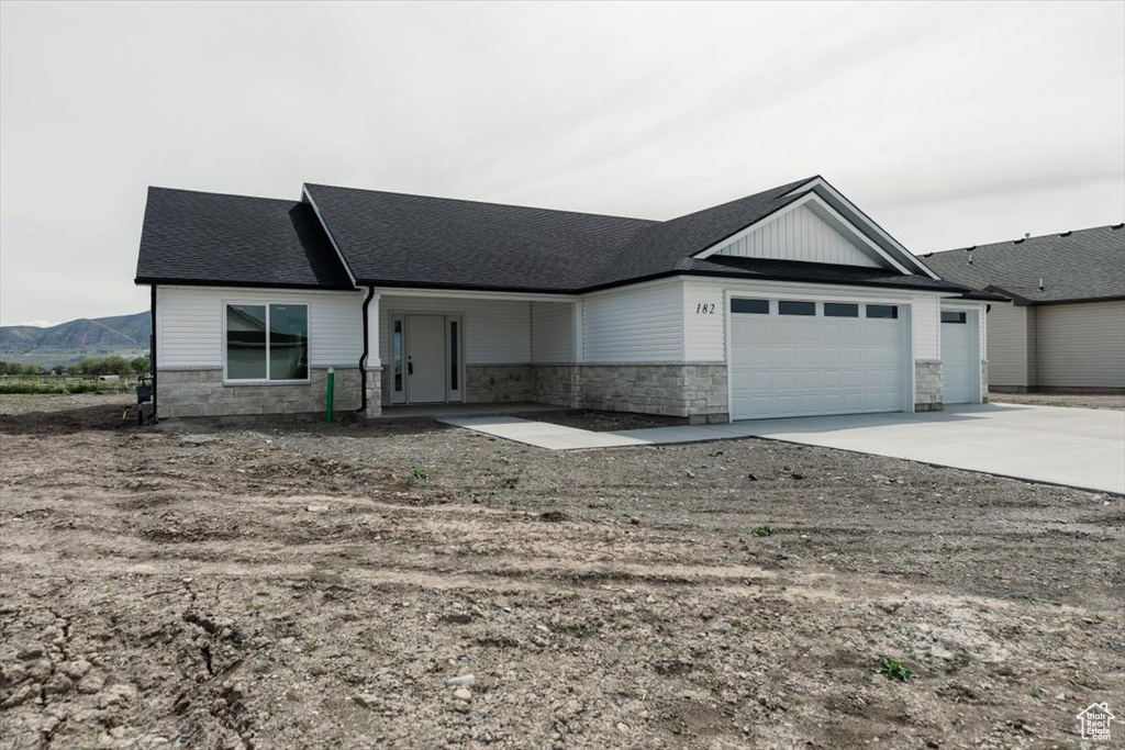 Ranch-style home featuring an attached garage, roof with shingles, stone siding, and concrete driveway