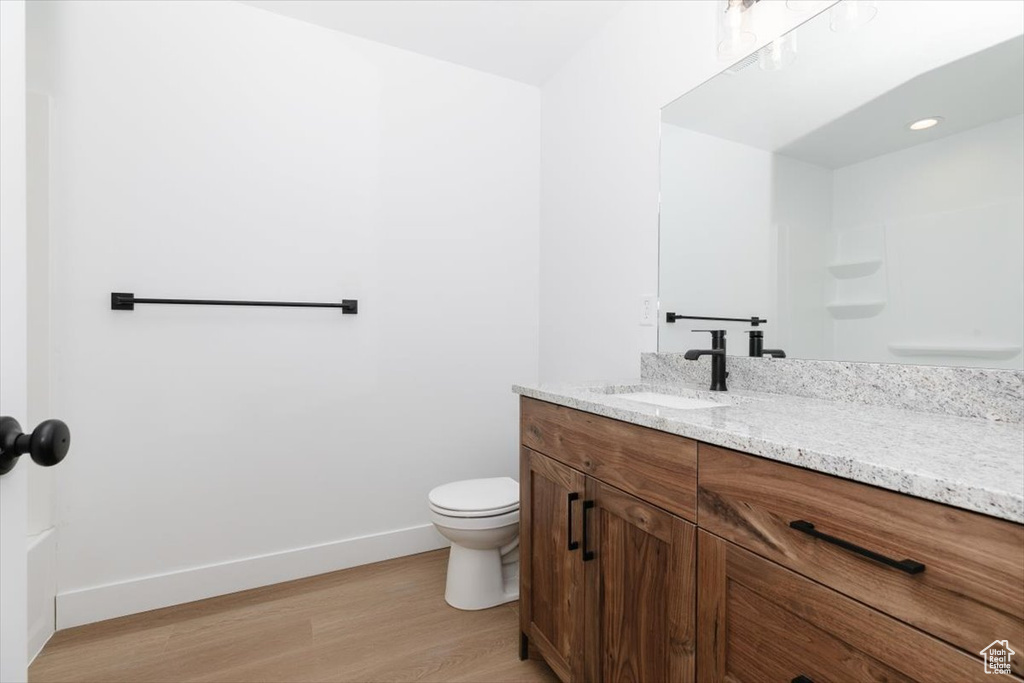 Bathroom featuring toilet, baseboards, wood finished floors, and vanity