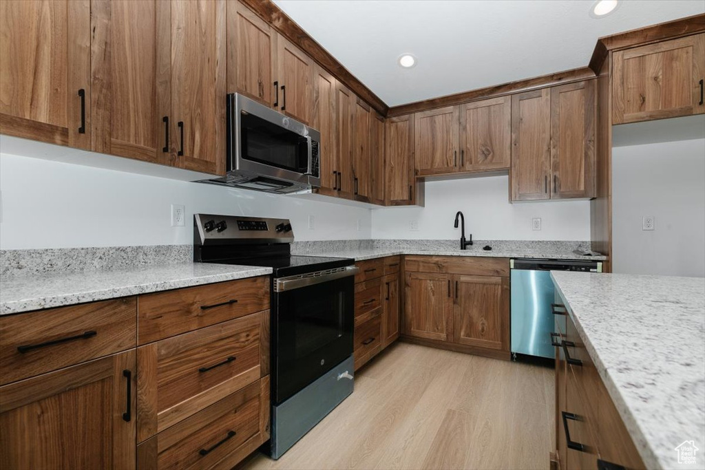 Kitchen with stainless steel appliances, brown cabinetry, a sink, and light wood-style floors