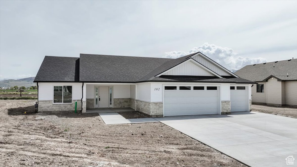 Ranch-style home with a garage, a shingled roof, driveway, and stone siding
