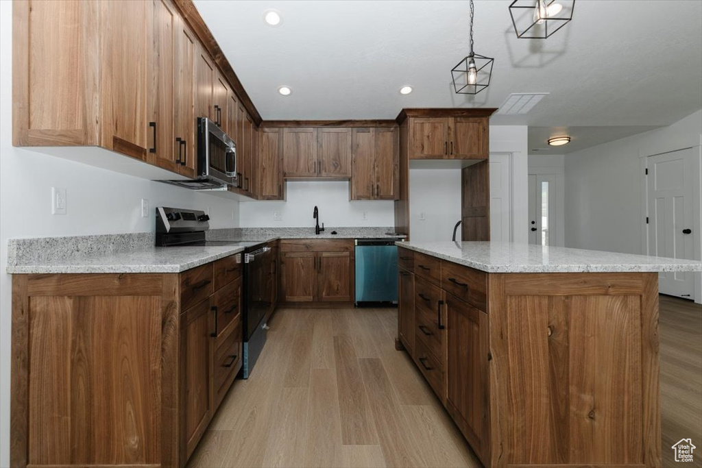 Kitchen with pendant lighting, stainless steel appliances, brown cabinets, and light wood-style flooring