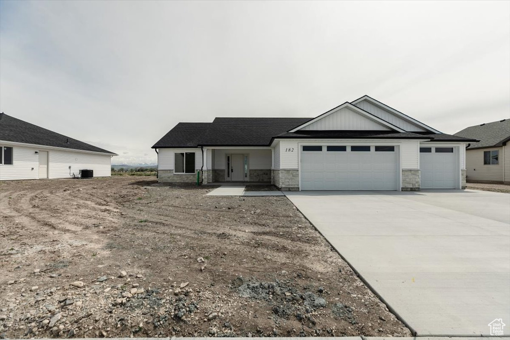 View of front facade featuring a garage, central air condition unit, stone siding, and concrete driveway