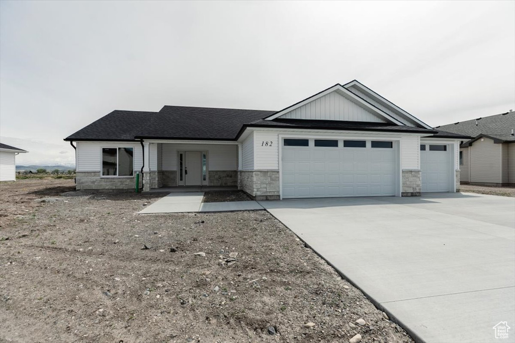 View of front of home featuring concrete driveway, roof with shingles, stone siding, and a garage