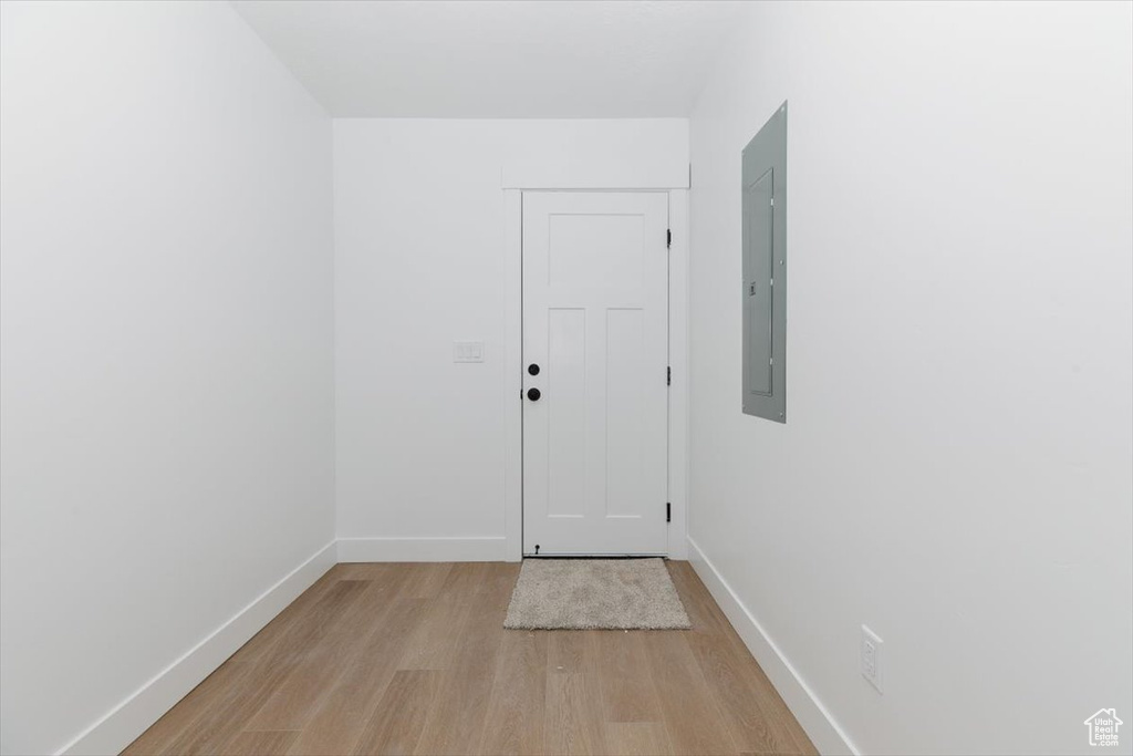 Doorway with baseboards, electric panel, and light wood-type flooring