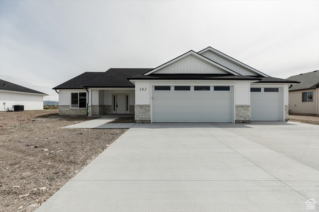 Craftsman inspired home featuring an attached garage, driveway, central AC, and stone siding