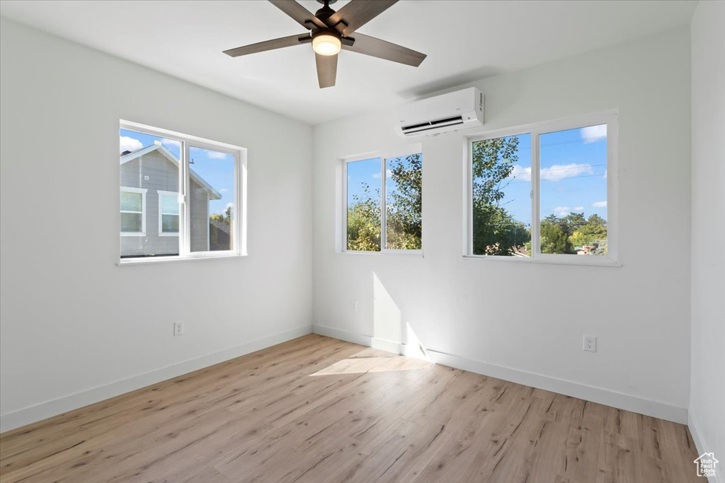 Unfurnished room with ceiling fan, baseboards, light wood-style flooring, and a wall unit AC