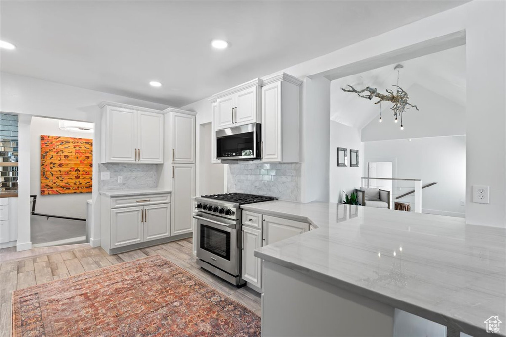 Kitchen with light stone counters, backsplash, stainless steel appliances, a peninsula, and white cabinets