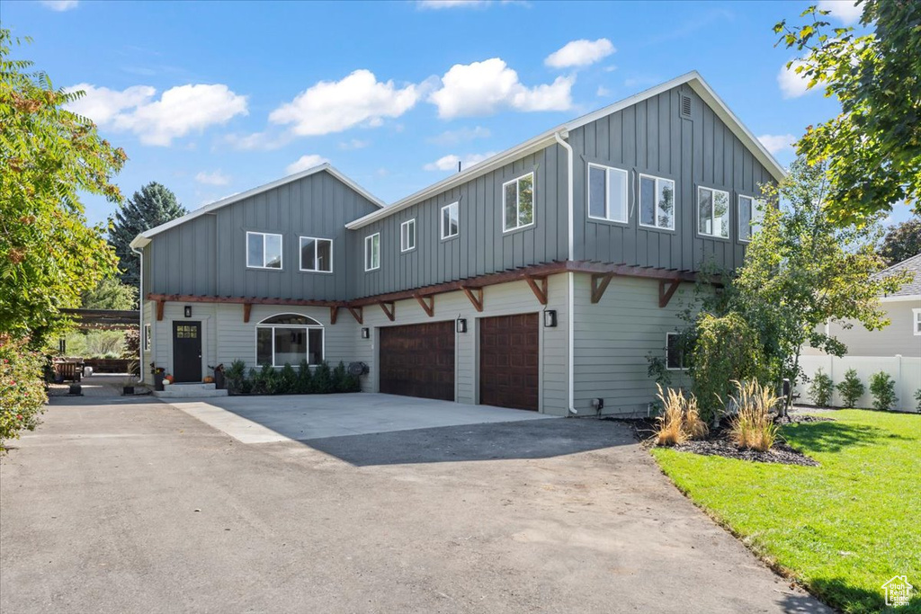 View of front of home featuring a front yard, fence, concrete driveway, a garage, and board and batten siding