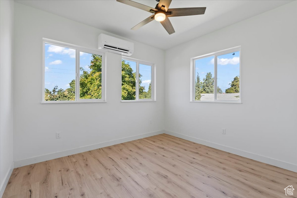 Empty room featuring light wood finished floors, baseboards, a wall mounted air conditioner, and ceiling fan