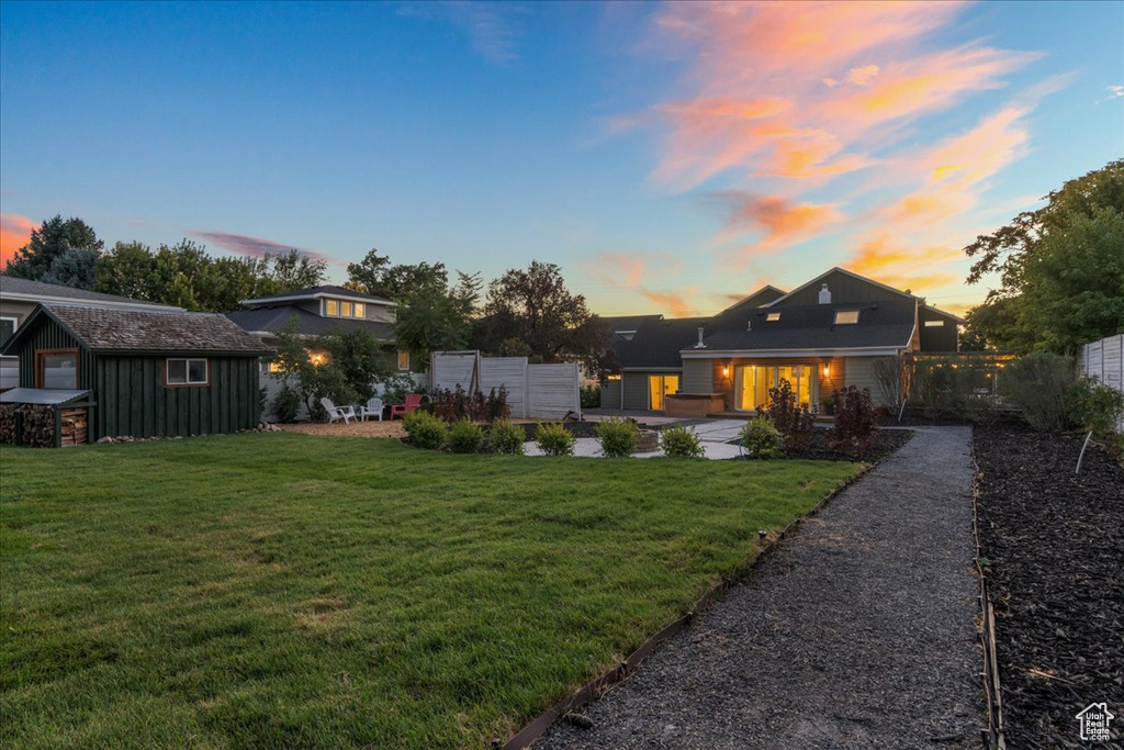 Back of property at dusk with a yard and fence