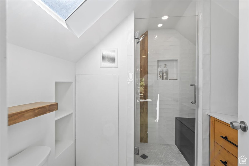 Full bath featuring vaulted ceiling with skylight, toilet, visible vents, and a stall shower