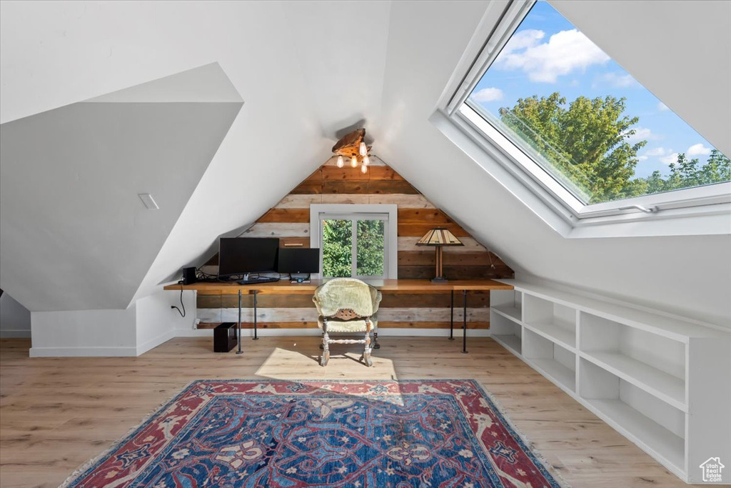 Interior space featuring lofted ceiling with skylight, built in shelves, wood finished floors, and wood walls