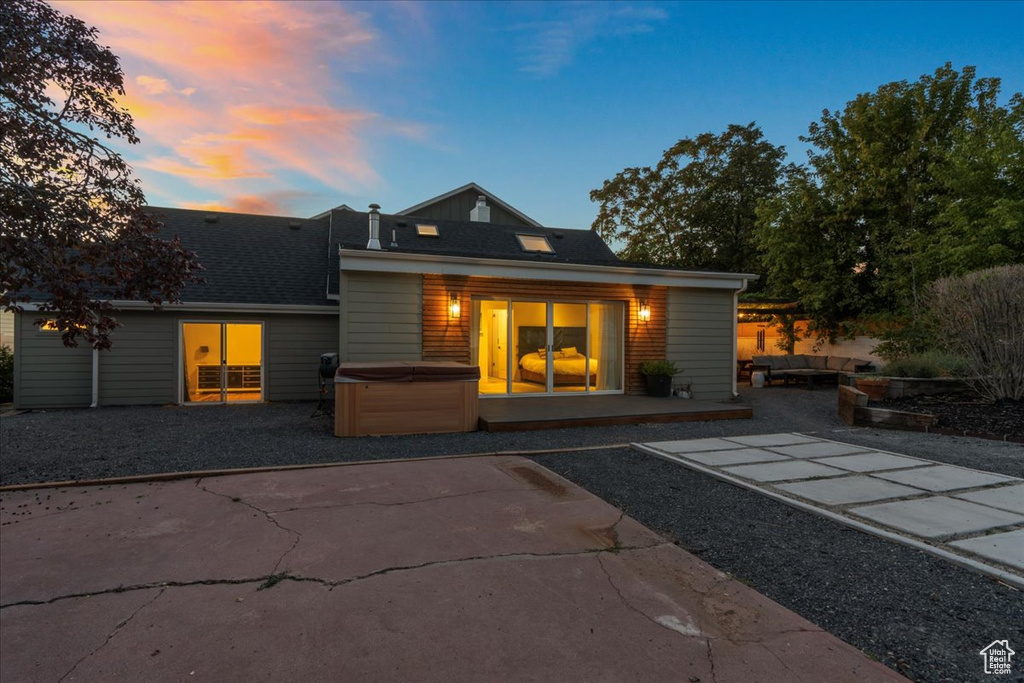 Back of house at dusk with a patio, a shingled roof, and a hot tub