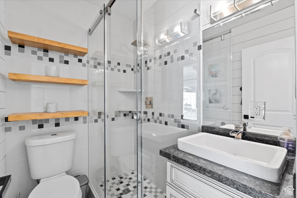 Bathroom featuring tasteful backsplash, a shower stall, toilet, vanity, and tile walls