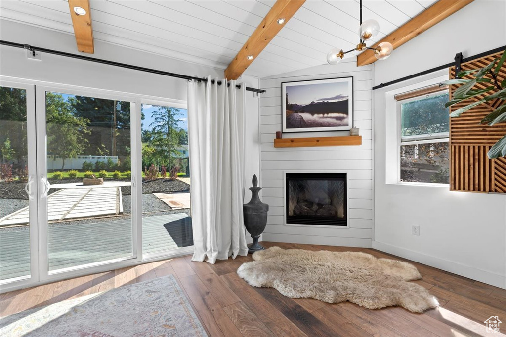 Unfurnished living room with hardwood / wood-style floors, vaulted ceiling with beams, a fireplace, and plenty of natural light