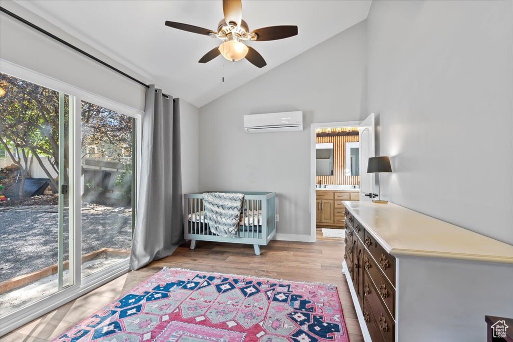 Living area with an AC wall unit, light wood finished floors, baseboards, ceiling fan, and vaulted ceiling