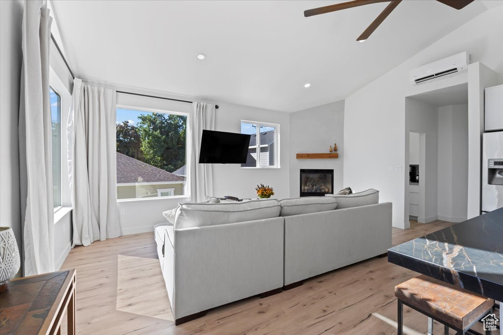 Living area featuring lofted ceiling, light wood-style flooring, ceiling fan, an AC wall unit, and a glass covered fireplace