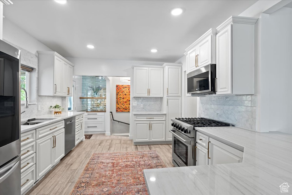 Kitchen with decorative backsplash, recessed lighting, light wood-style floors, white cabinets, and stainless steel appliances
