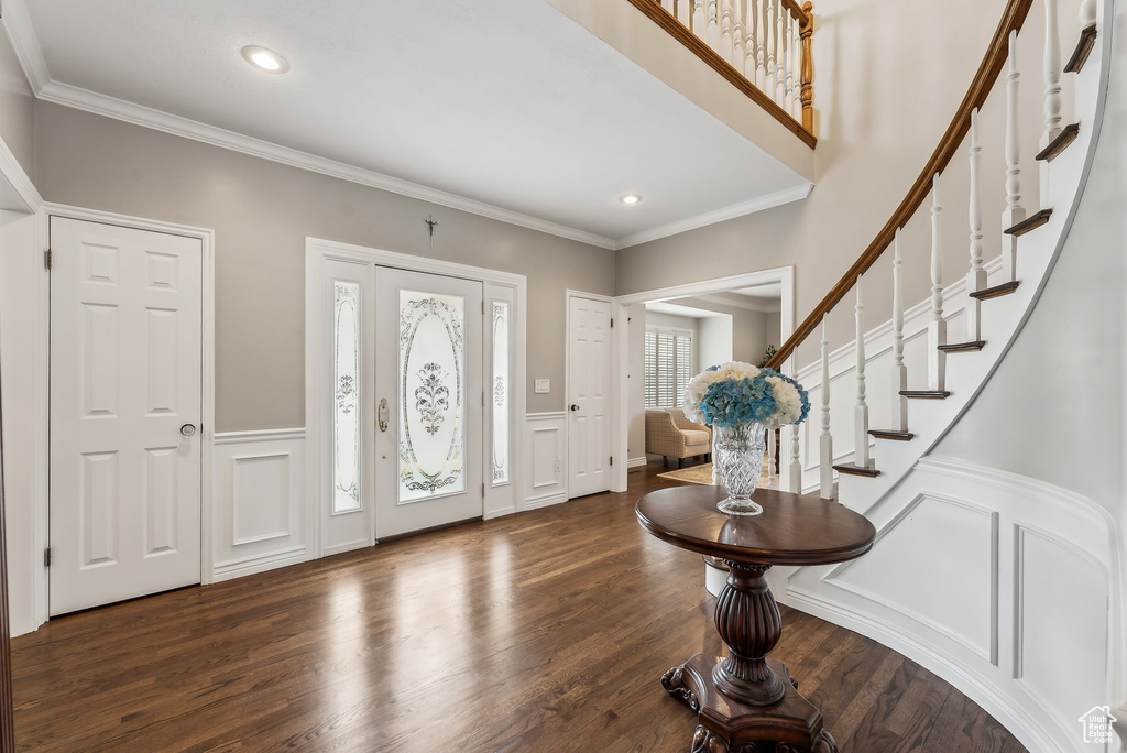 Entrance foyer featuring stairs, dark wood-type flooring, crown molding, and a decorative wall