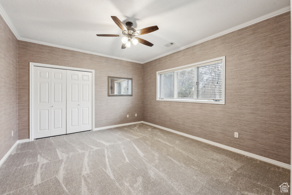 Unfurnished bedroom featuring a closet, carpet flooring, crown molding, baseboards, and ceiling fan