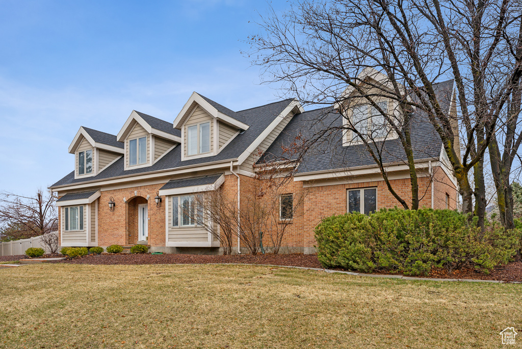 Cape cod-style house with brick siding, a front yard, and roof with shingles